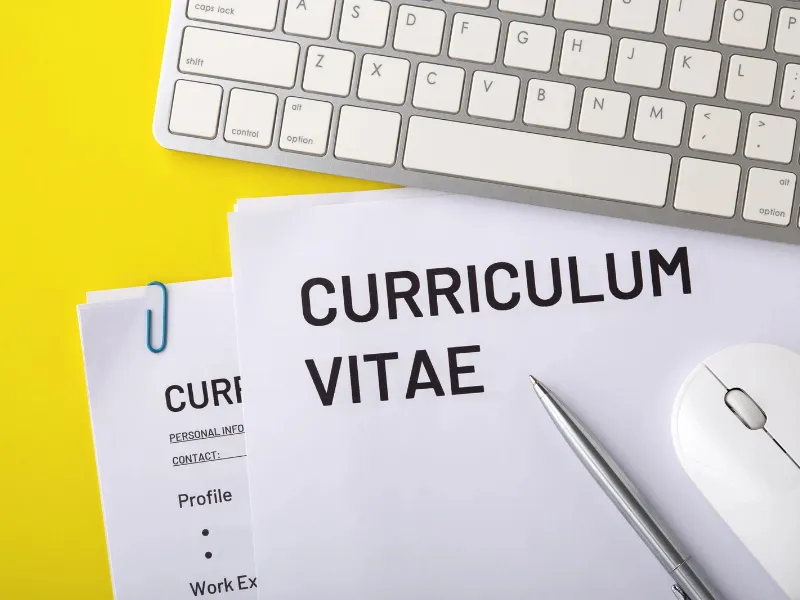 Currículum vitae impreso sobre un escritorio junto a un teclado y una pantalla de ordenador