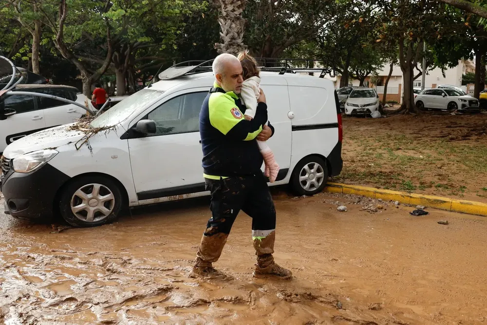 Un miembro de transporte sanitario con una niña tras las intensas lluvias en Picaña (Valencia). EFE - Biel Aliño